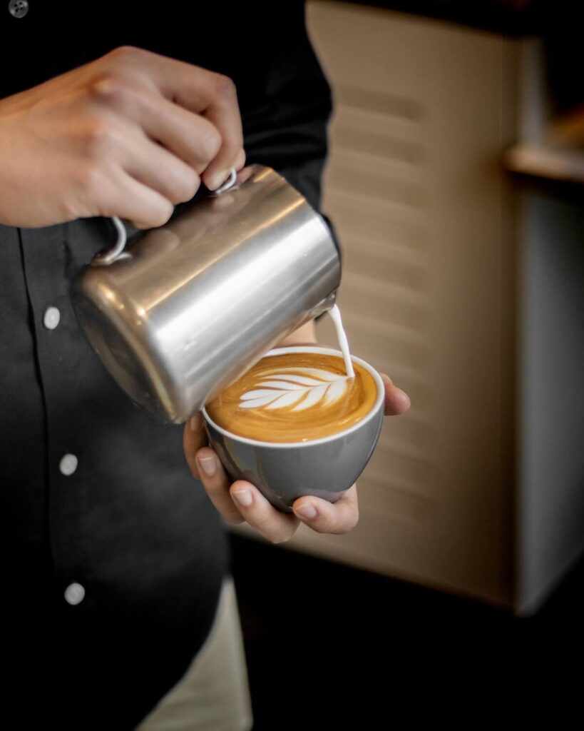 barista pouring milk over flat white
