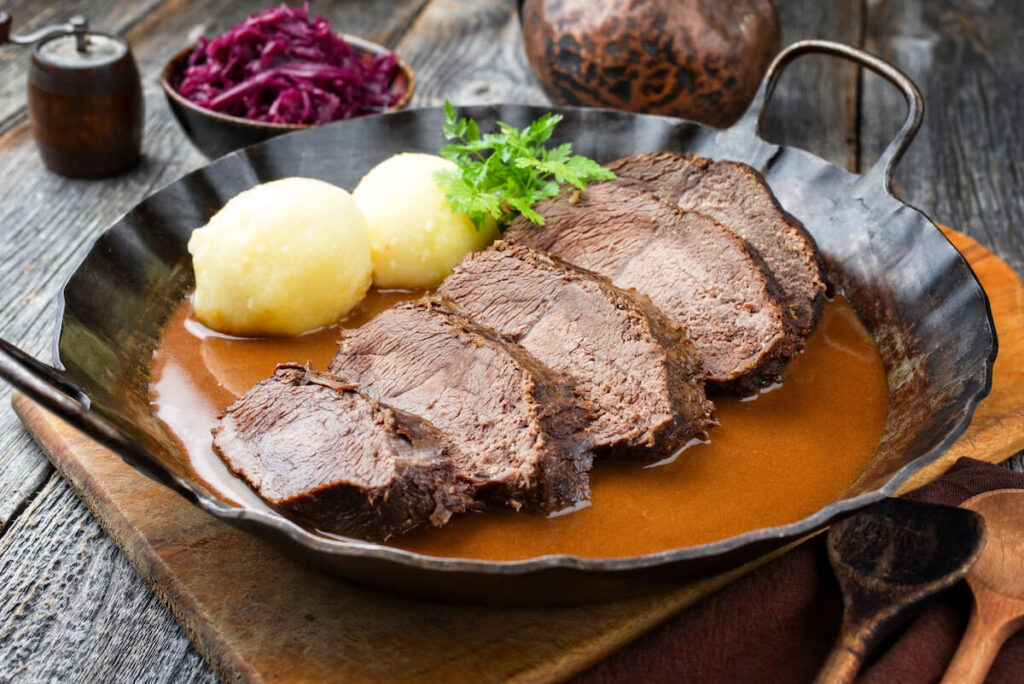 Traditional braised marinated German Sauerbraten from beef with potato dumplings and blue kraut in spicy brown sauce