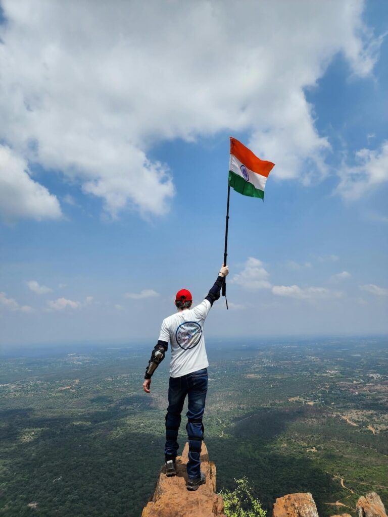 man holding Indian flag on top of a mountain