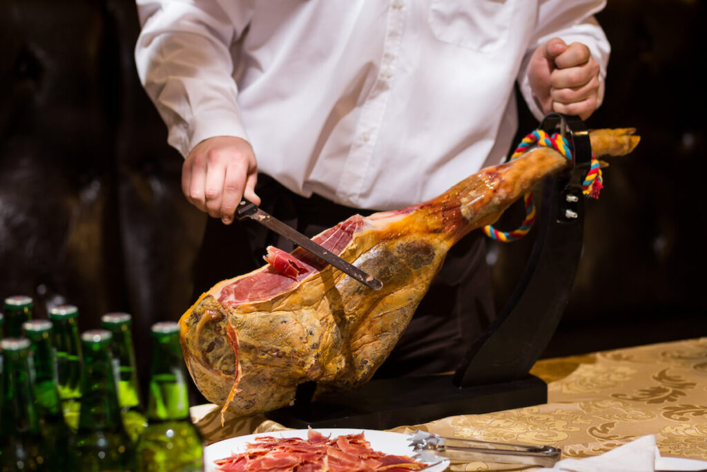 The waiter is cutting slices the jamon on a wooden stand
