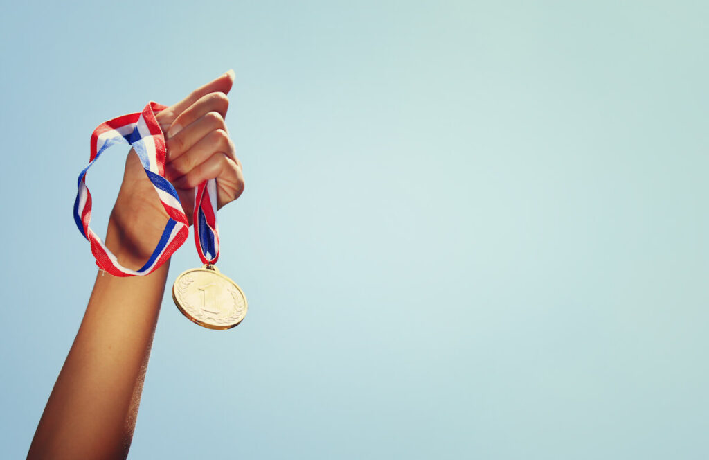 woman hand raised, holding gold medal against sky