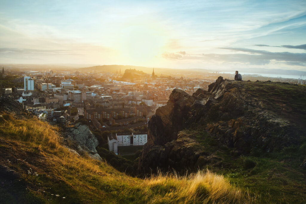 Top view from the mountains of Edinburgh and a seated tourist looking out over the city at sunset from Arthur's Seat, Edinburgh