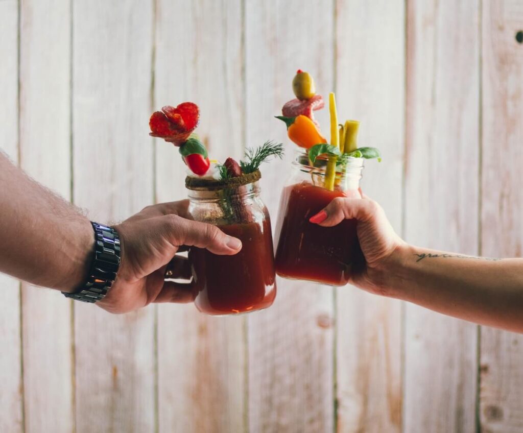 two people clinking glasses full of red drink and colorful garnishes