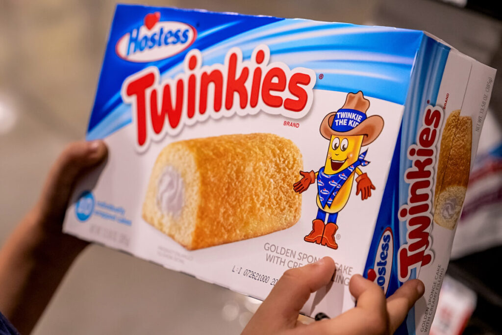 Childs hand holding a box of Twinkies brand cream filled cakes in a supermarket aisle