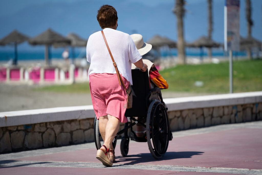 A woman pushes another one in a wheelchair in Malaga's oceanside