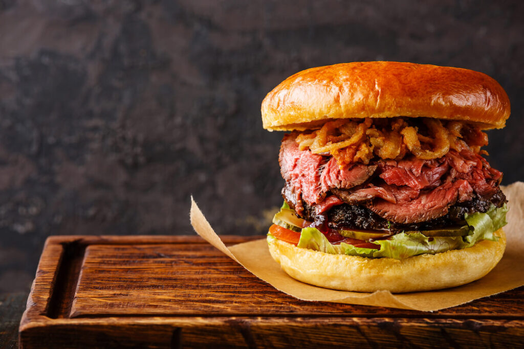 Pastrami Burger with sliced Roast beef and onion fries rings on black background