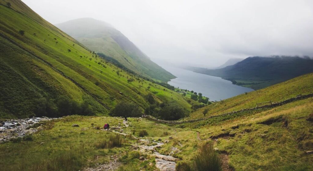 Path winds down green mountain to lake in cloudy valley