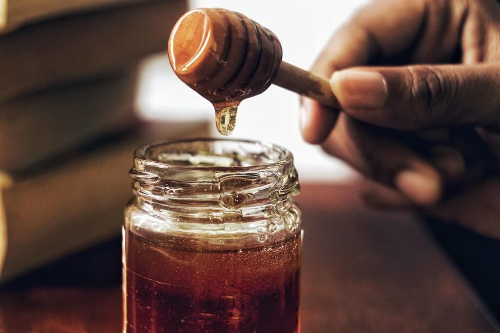 hand holding honey dipper on to bottle of honey