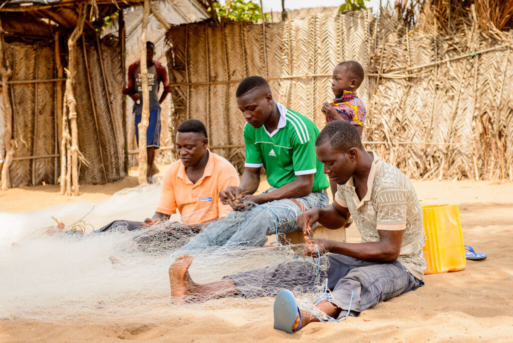 Unidentified Togolese men sew the fish net for fishing. Togo is known for its fishing industry.