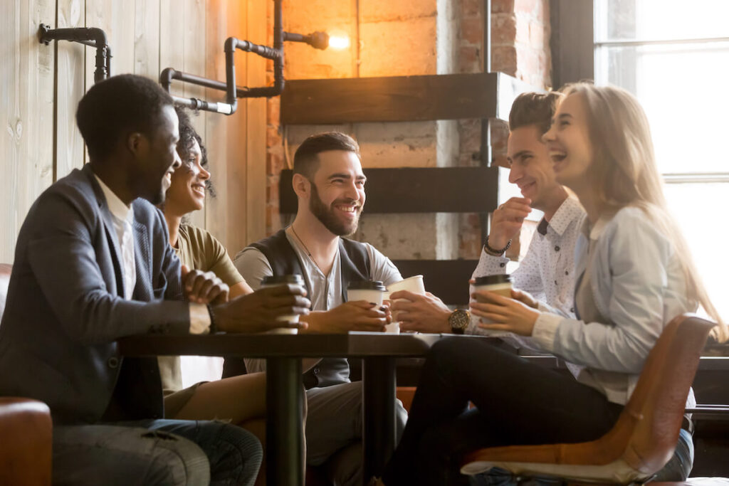 young people talking joking sitting together at cafe table
