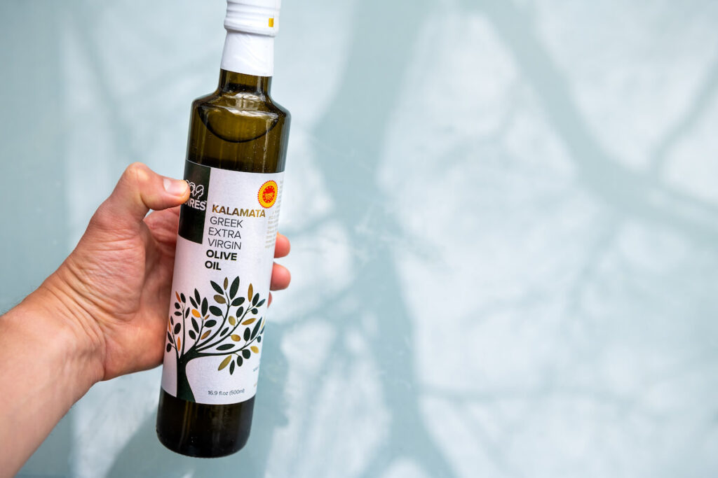 Closeup of hand holding Moires PDO Kalamata EVOO Kalamata greek extra virgin olive oil bottle and sign label