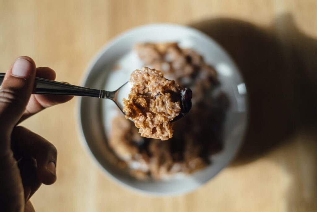 hand holding spoon of raisin bran cereals with milk