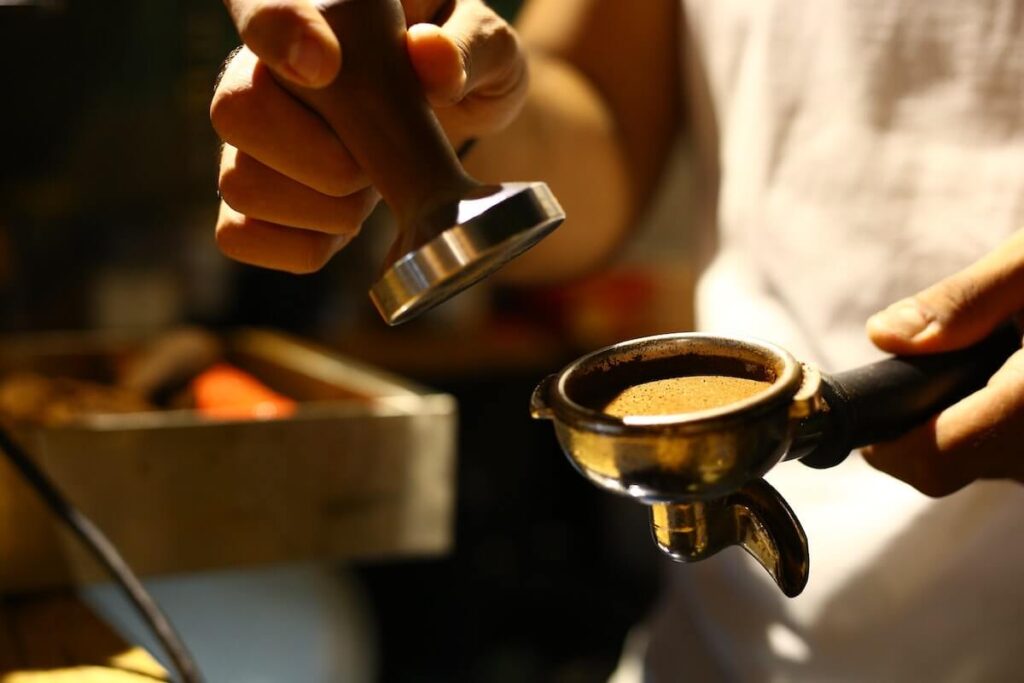 barista stamping coffee grounds to make espresso