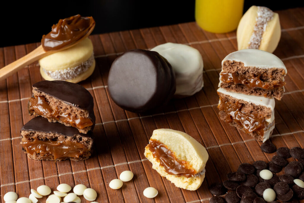 Artisanal alfajores of cornstarch with coconut, white chocolate and dark chocolate with dulce de leche on wooden mat