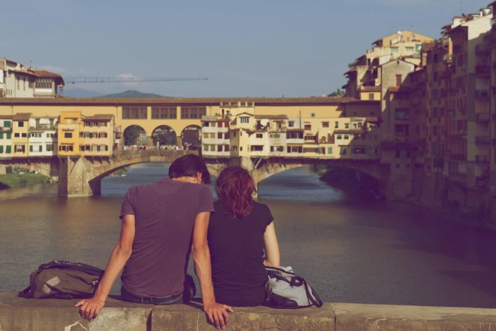 couple sitting on ponte santa trinita overlooking ponte vecchio