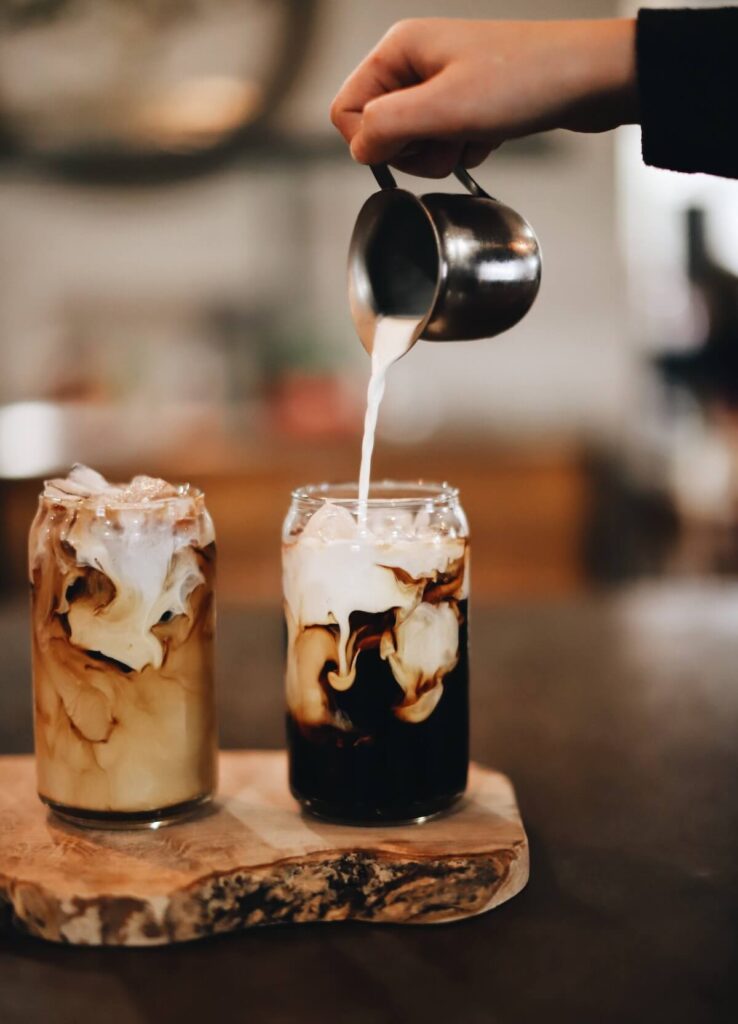 pouring milk over iced black coffee