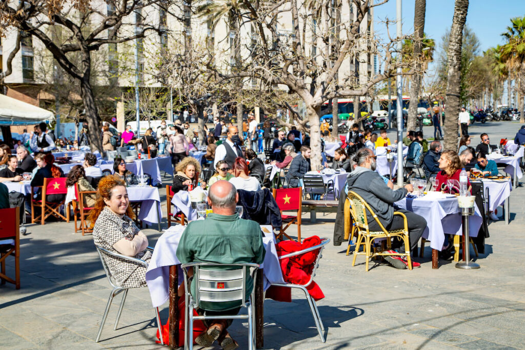 People dine on the open verandas of cafes and restaurants on the Barceloneta promenade