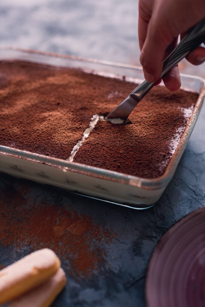 hand holding knife cutting through tiramisu