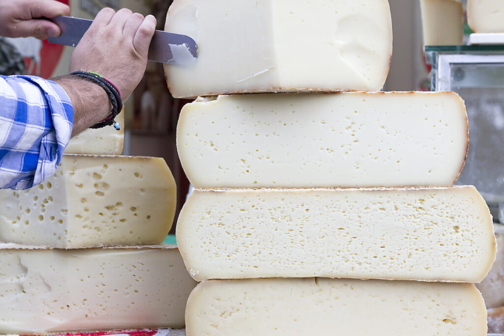 A stack of traditional, large Cretan graviera cheeses on display at a farmers' market
