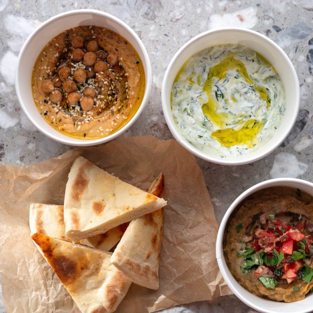Pita with assorted traditional greek dips, tzatziki, vegetable caviar, hummus over light background