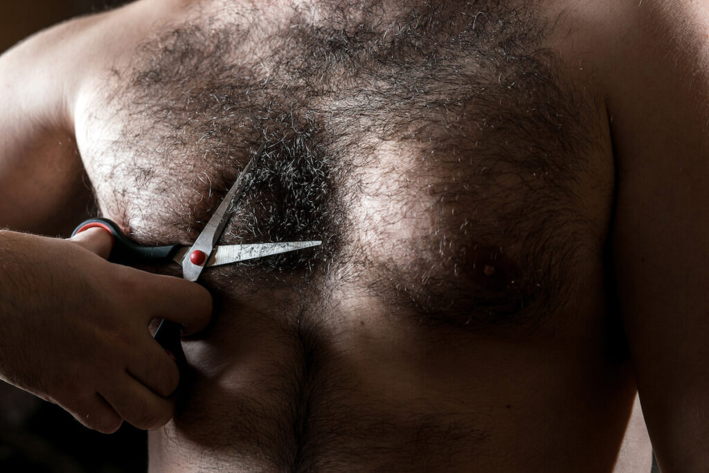 man with scissors cuts the hair on his hairy chest