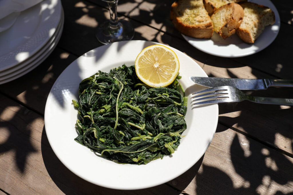 Cooked greens salad served with lemon and olive oil on a white dish