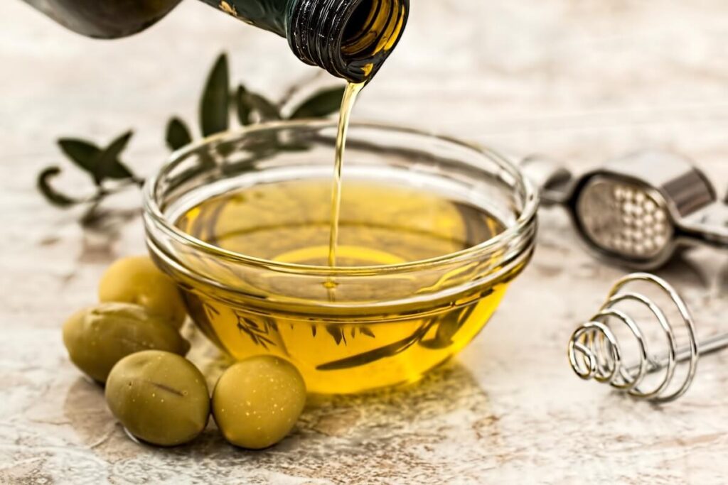 small bowl of olive oil with fresh olives beside it