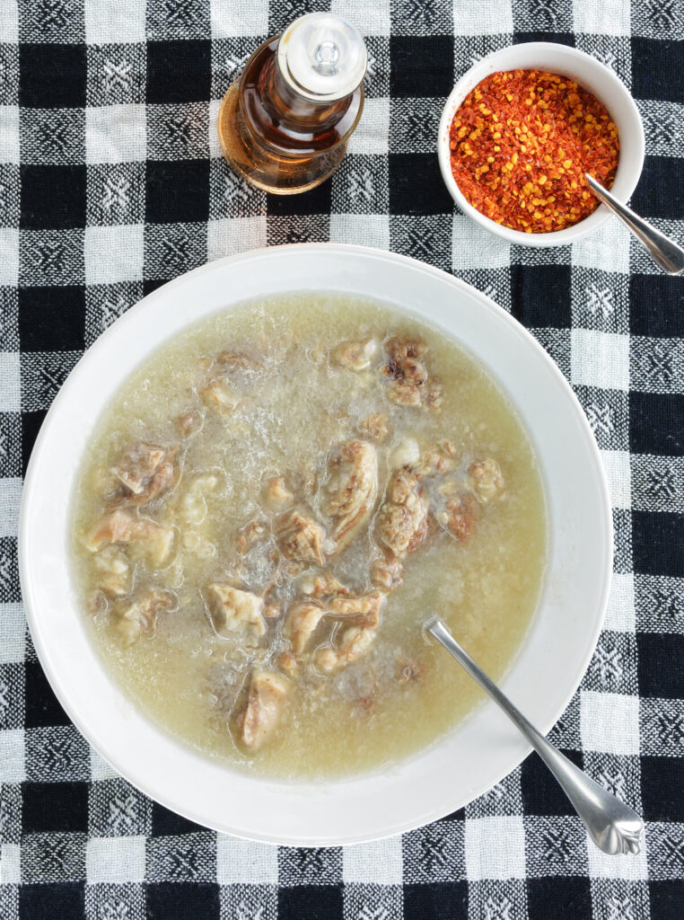 Patsa the traditional greek soup with a bottle of vinagar and chopped garlic and crashed red hot chilli pepper on check tablecloth