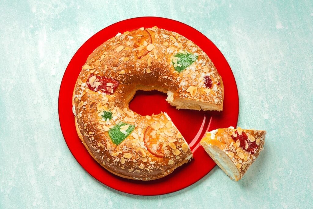Top view of roscon de reyes with cream and Christmas ornaments on a red plate over light blue background