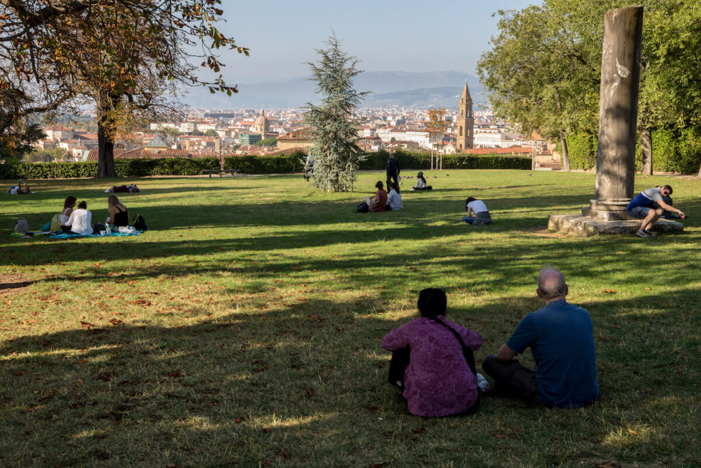 People, young and old, are sitting or lying on grass in Boboli Gardens, overlooking the historic center of town, on a sunny afternoon