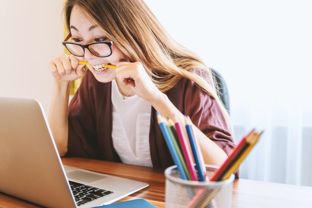 woman biting a pen while looking at the laptop screen