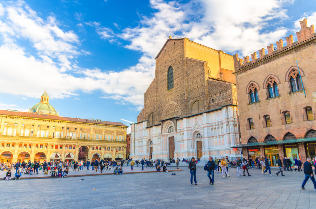 Basilica di San Petronio church and Palazzo dei Banchi palace building on Piazza Maggiore square and many walking people in old historical city center