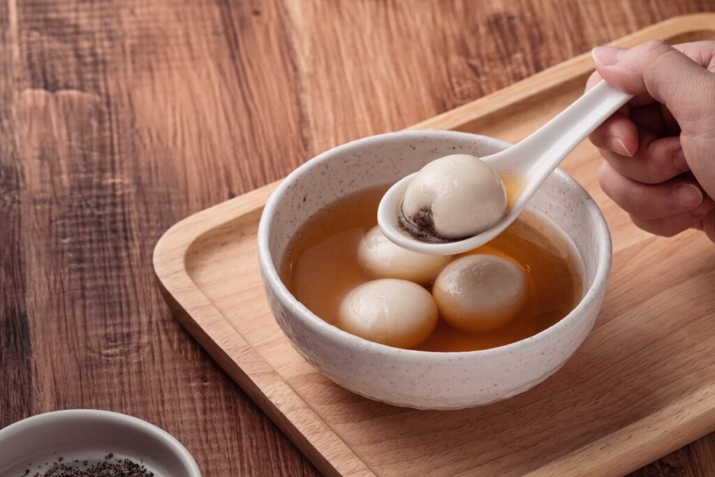 Close up of sesame big tangyuan (tang yuan, glutinous rice dumpling balls) with sweet syrup soup in a bowl on wooden table background