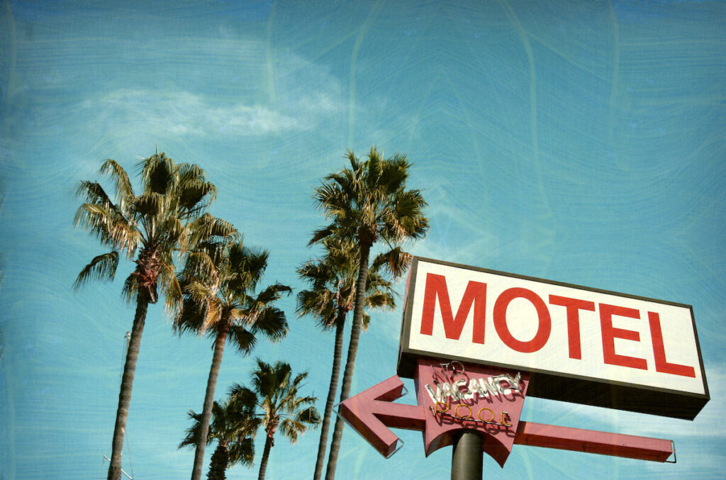 aged and worn vintage photo of motel sign with palm trees in the background