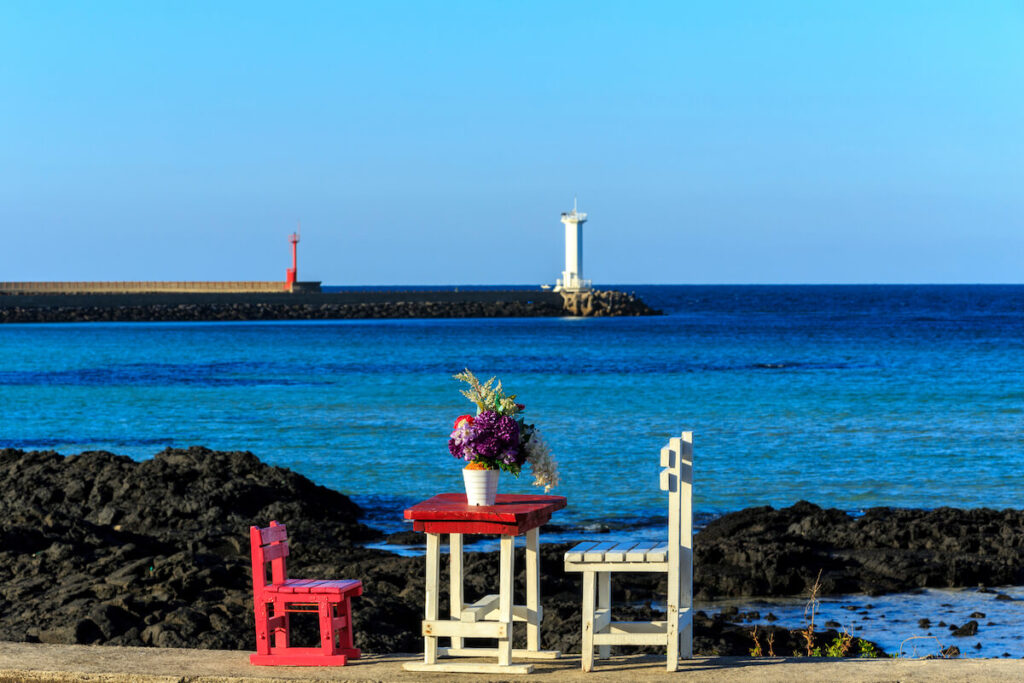 A wooden desk and two chairs with flower vase are on the concrete in Sehwa Beach