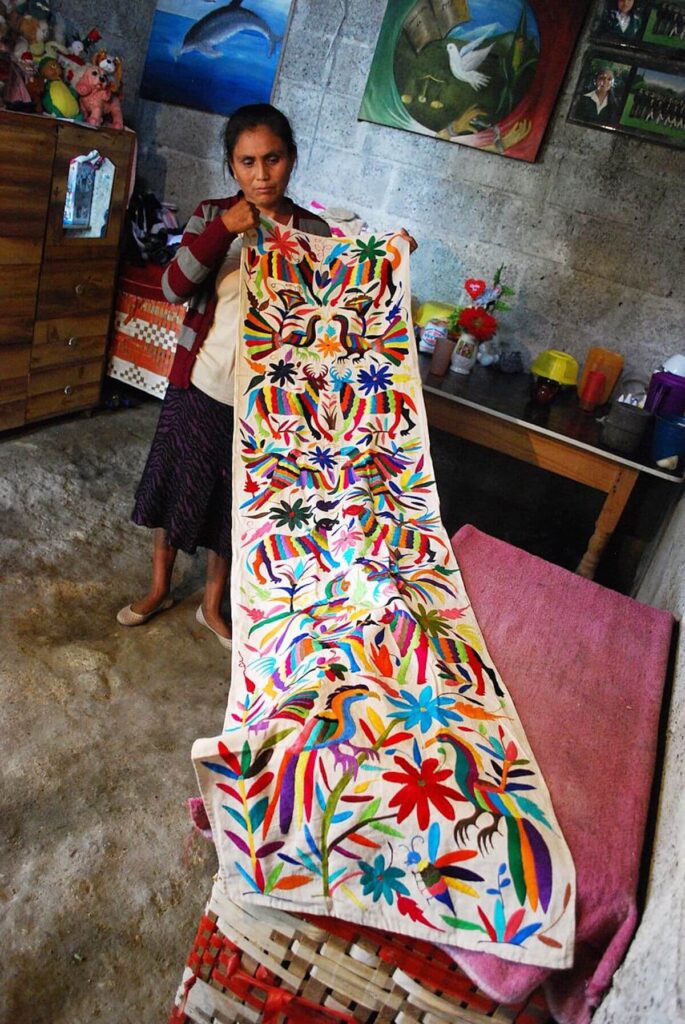Mexican artisan shows Tenango embroidered piece in studio