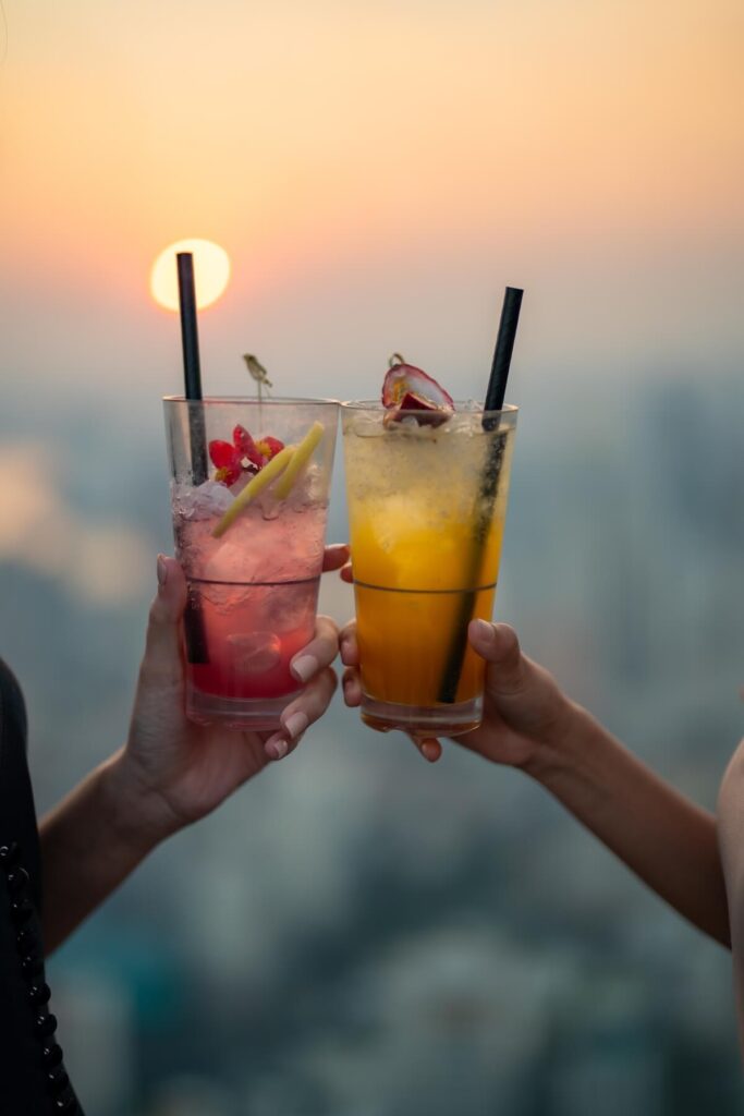 friends meeting and drinking cocktail together at skyscraper rooftop restaurant in metropolis