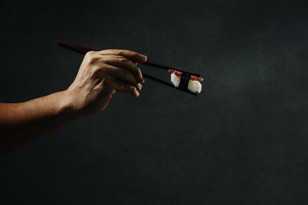 person holding chopsticks with sushi