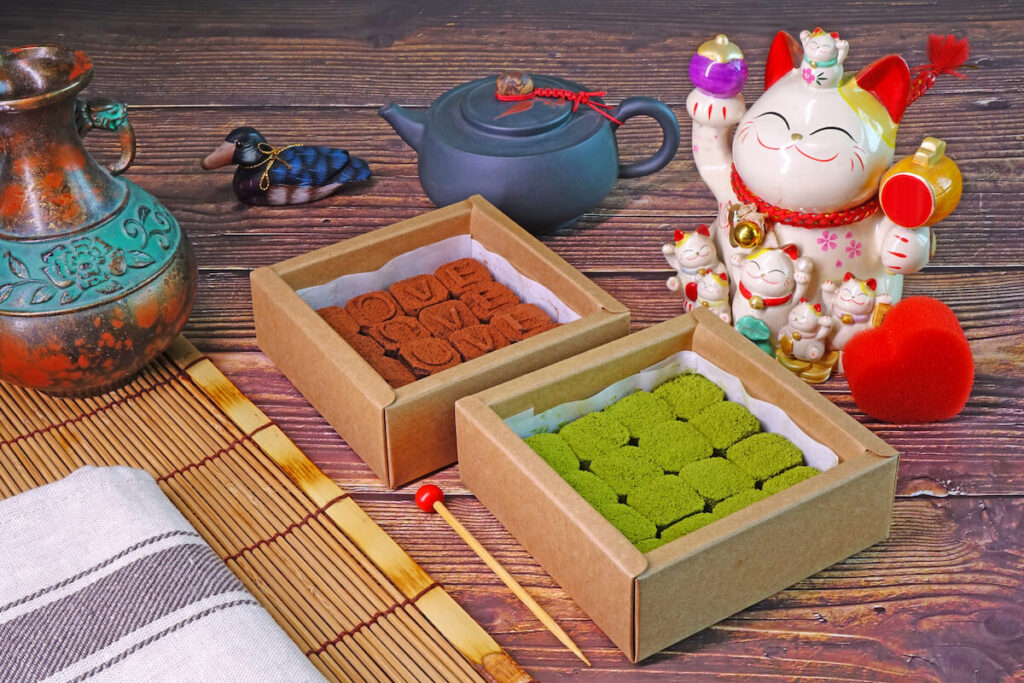 assorted souvenirs from Japan including nama chocolates, Maneko Neko, teapot, and lucky charms on table