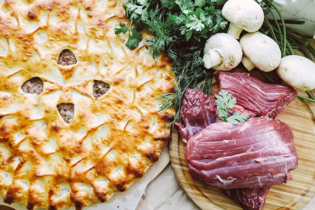 Raw meat on a cutting board, a pie and mushrooms
