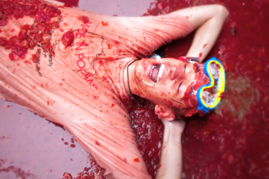 man lies and laughs in crushed tomatoes during La Tomatina Festival