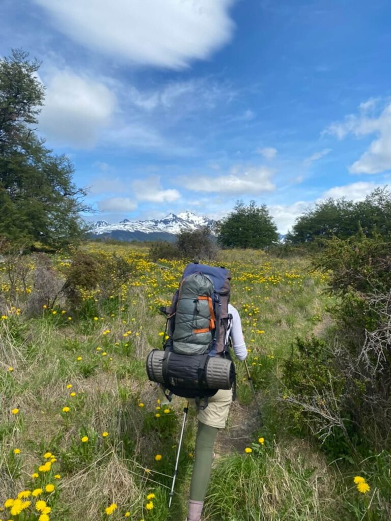 man with a hiking bag hiking through flowery route