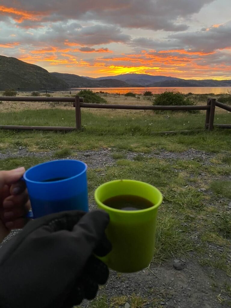 hands holding two plastic mugs of coffee while watching sunrise