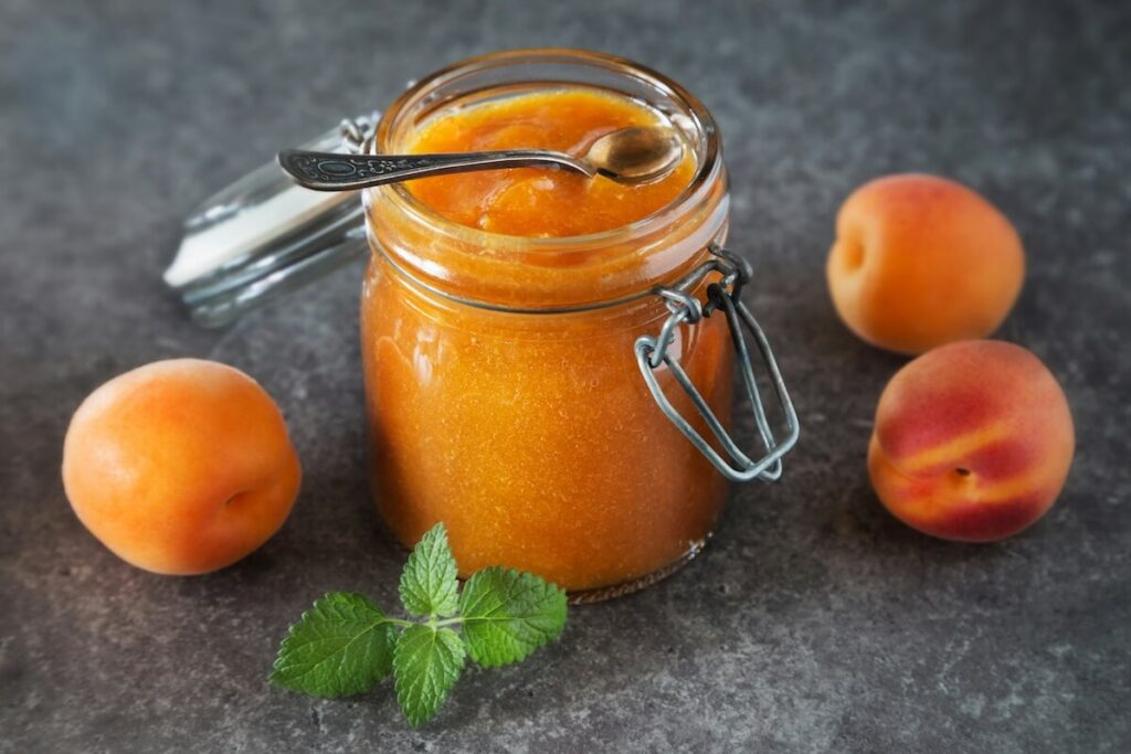 a bottle of apricot jam, with fresh apricots and peaches