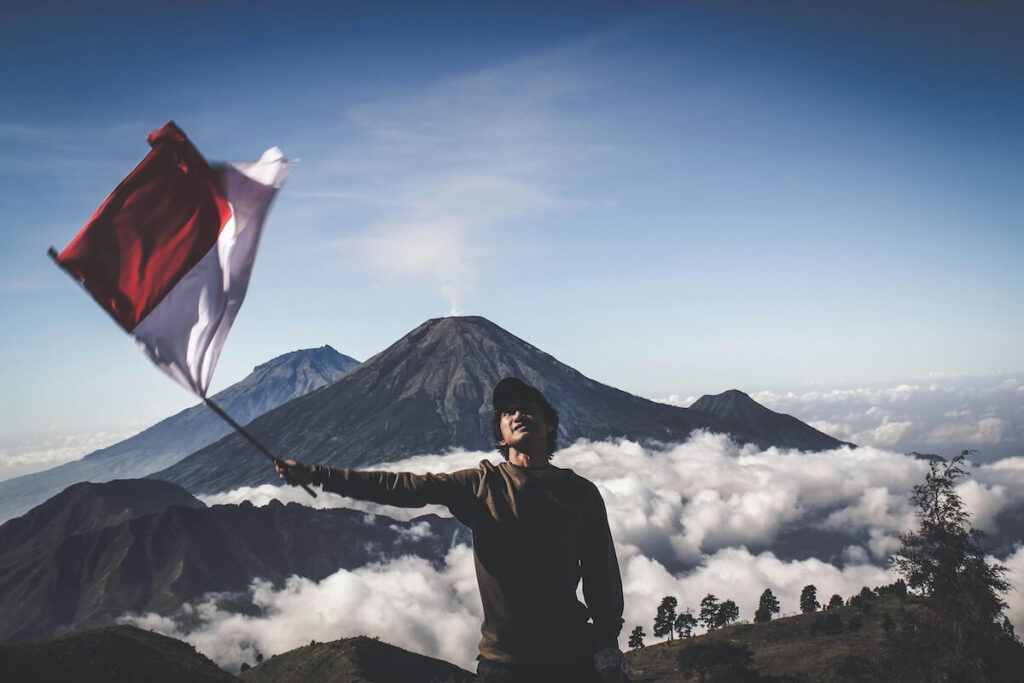 man holding Indonesian flag, with volcano in the background