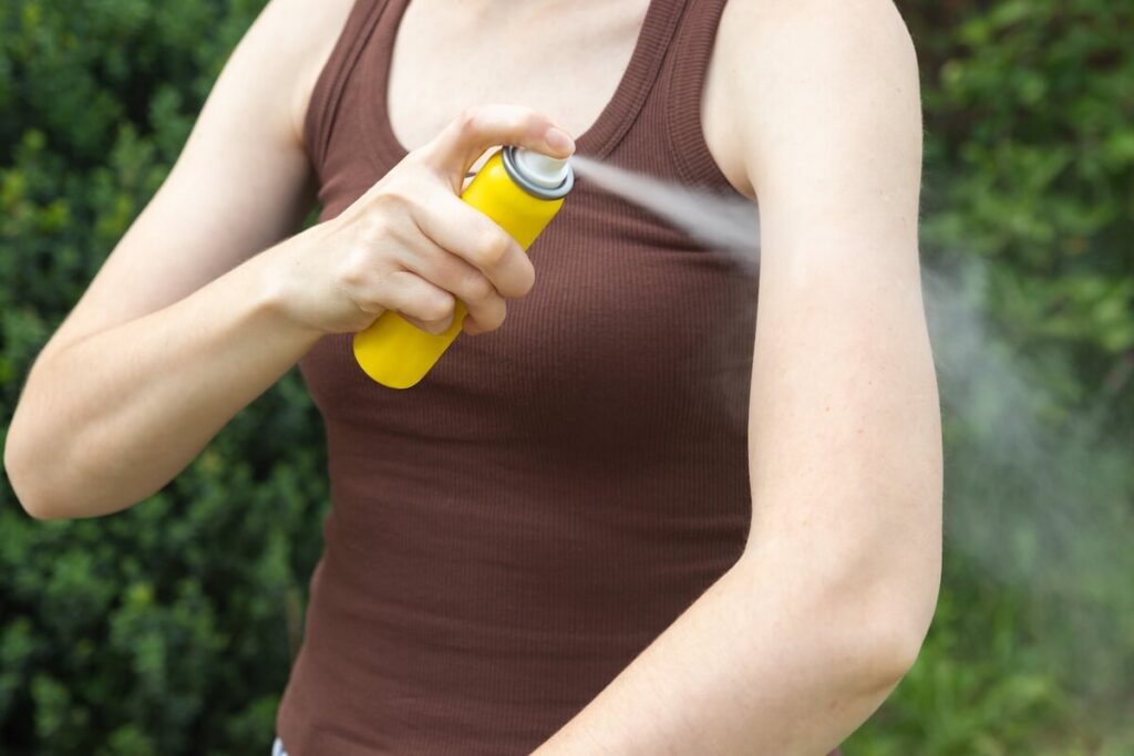 woman spraying insect repellent on arm