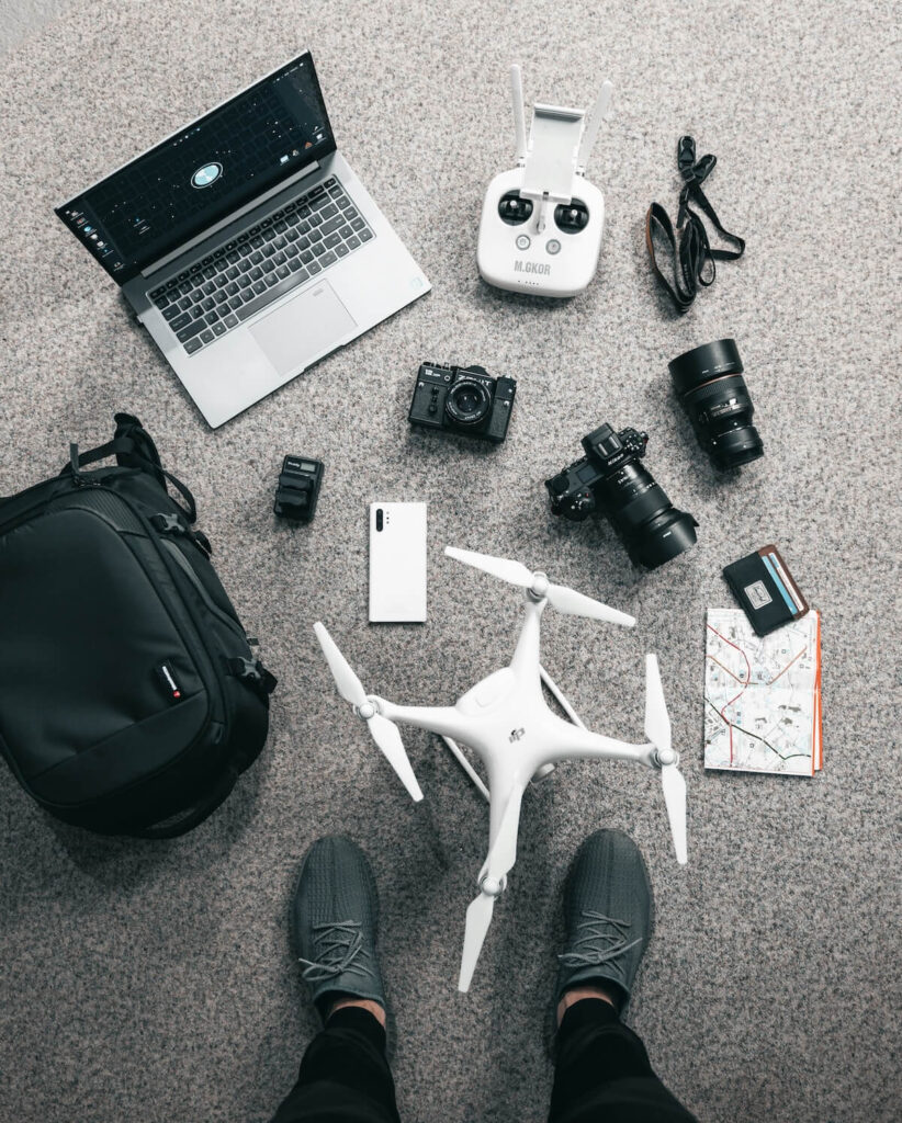 a laptop, a drone, drone controller, cameras, and other travel-related items laid out on floor
